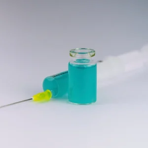 A glass vial and a syringe on a pale surface